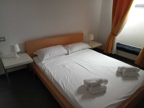 Ein Hotelzimmer mit einem Bett, einem Nachttisch mit Lampe und einem Fenster mit Vorhängen.