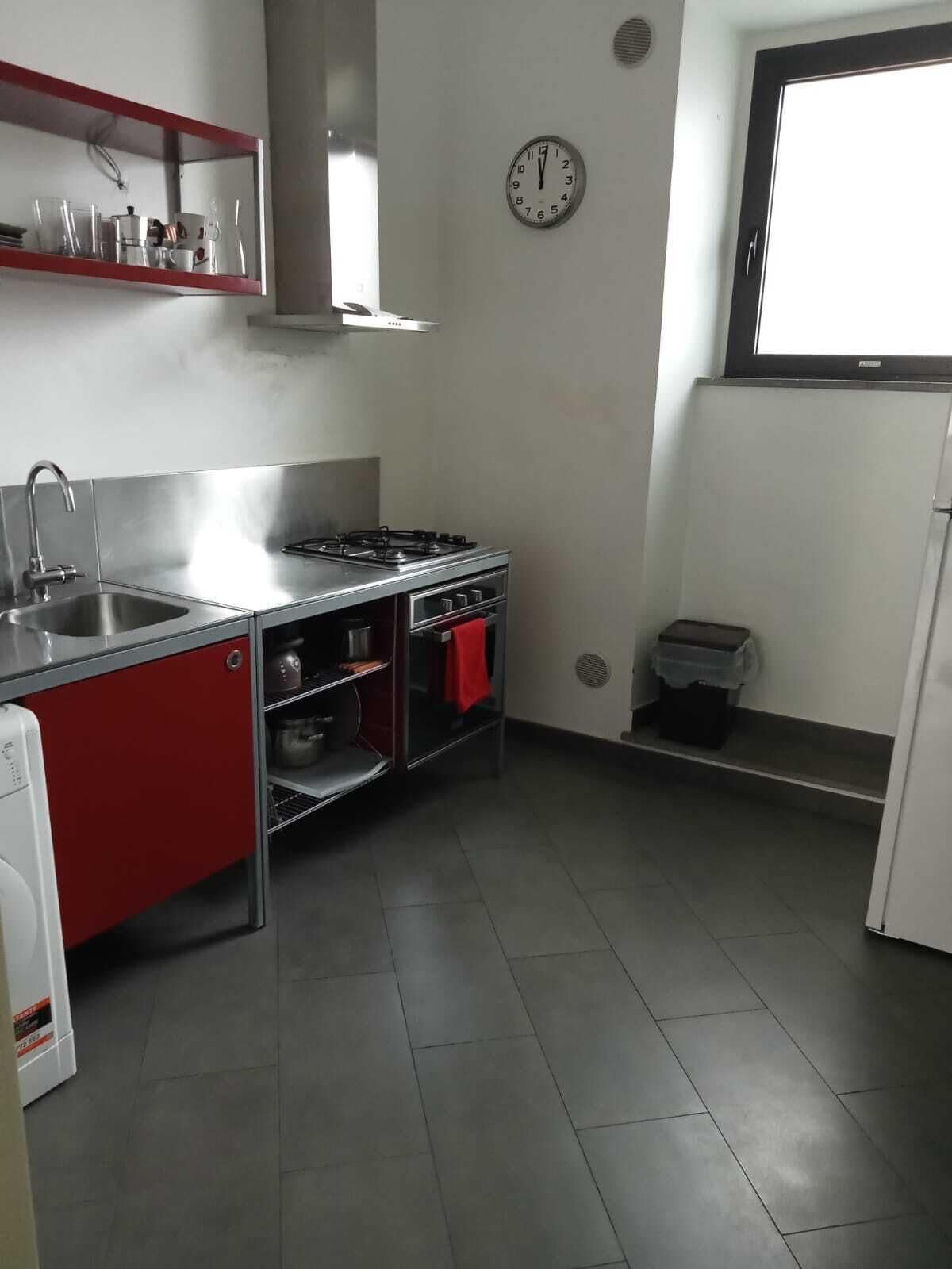 Eine kleine Küche mit Spüle aus Edelstahl, einem Gasherd und einem roten Schrank.