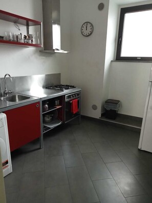 Una cocina compacta con un lavamanos de acero inoxidable, una estufa a gas y un armario rojo.