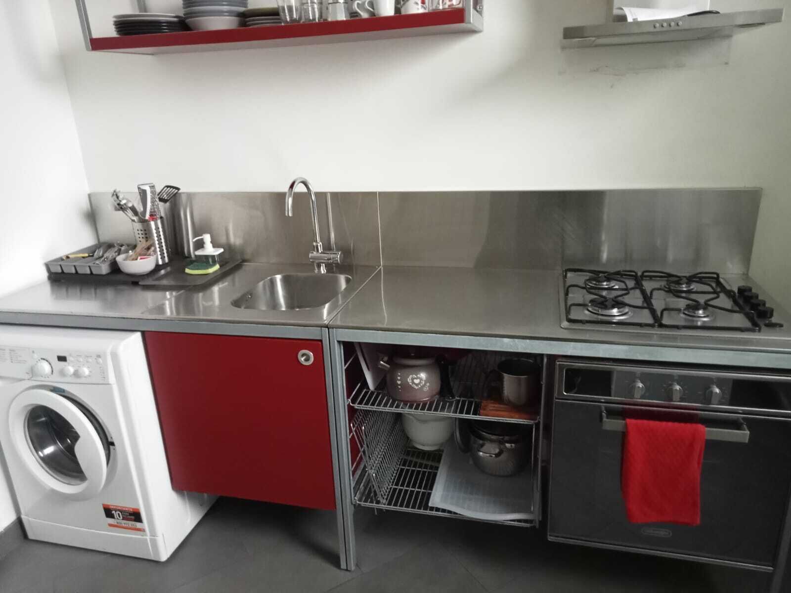 A compact kitchen with a stainless steel sink, a gas stove, a built-in washing machine, and a red cabinet.