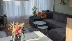 A modern living room with a sofa, a dining table, and a hanging light fixture. - Beach Resort Kamperland - 246 by Interhome (Kamperland)