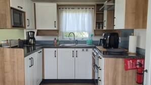 A compact kitchen with white cabinets, a stainless steel sink, a coffee maker, and a fire extinguisher. - Beach Resort Kamperland - 246 by Interhome (Kamperland)