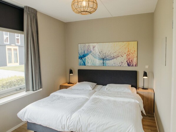 A bedroom with a bed, two bedside tables, a wall-mounted artwork, and a window with curtains.