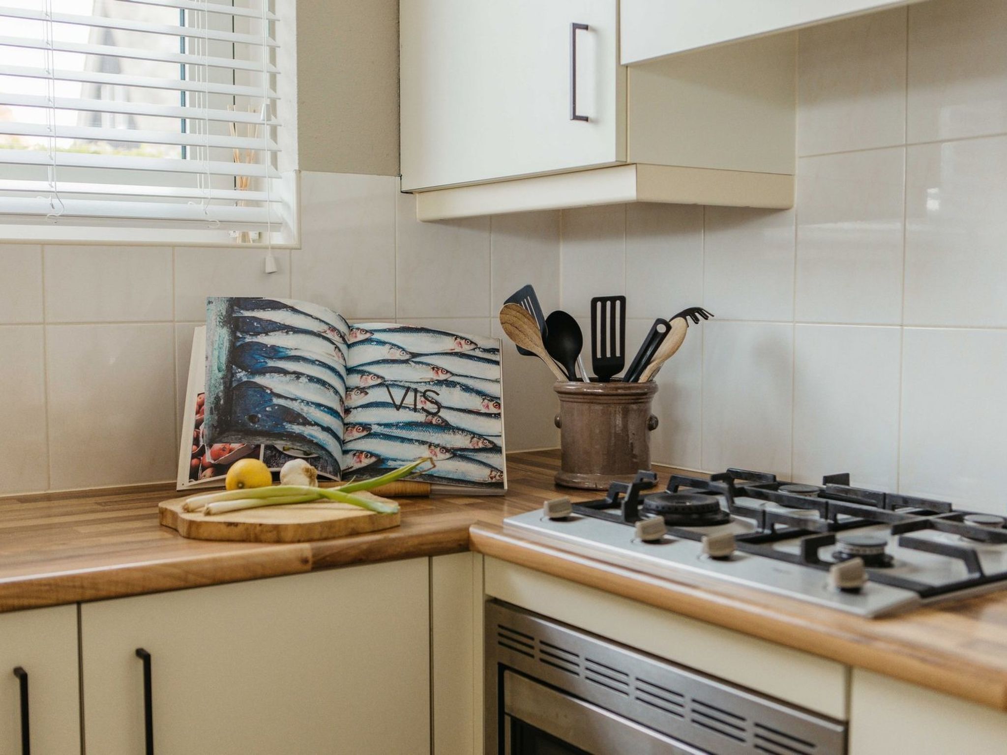 Una cocina con estufa a gas, tabla de cortar con verduras y un libro con ilustraciones de pescado.
