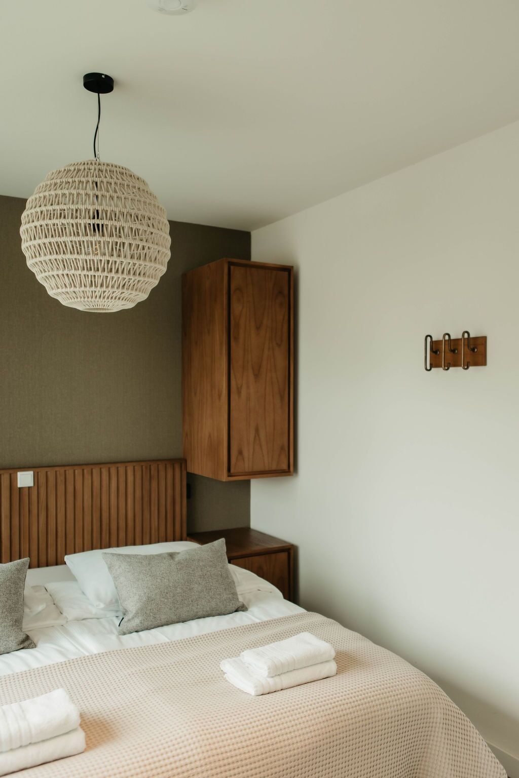 Un dormitorio con una cama, una lámpara colgante, un armario de madera y un perchero en la pared.