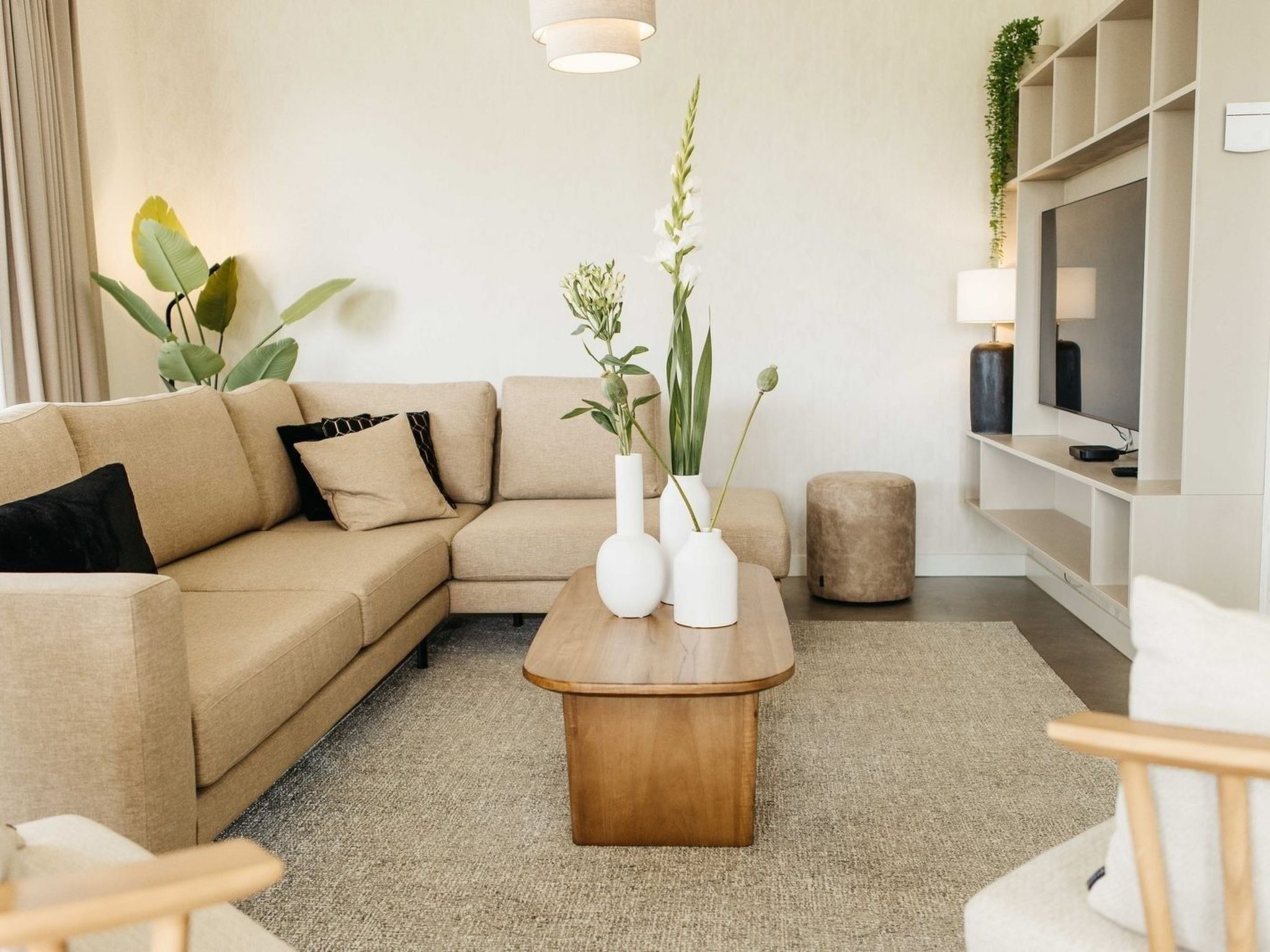 Un salón moderno con un sofá beige, una mesa de centro de madera y un televisor sobre un mueble blanco.