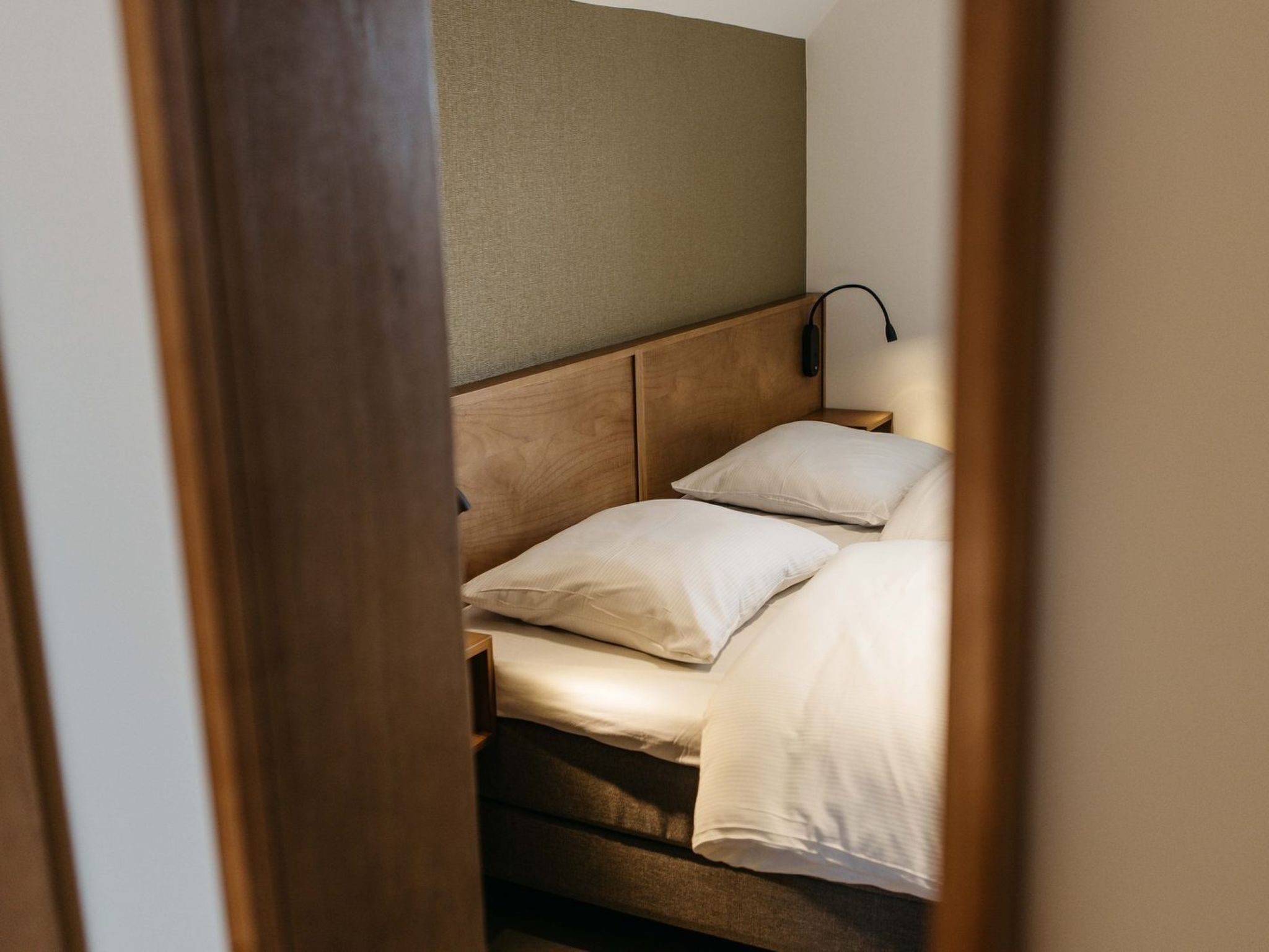 Una cama individual con cabecera, una lámpara de noche y un aplique de pared.