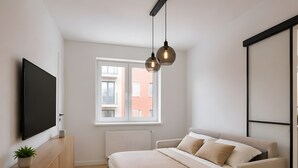 Une chambre moderne avec un lit, une télévision, une plante et une fenêtre donnant sur des immeubles.