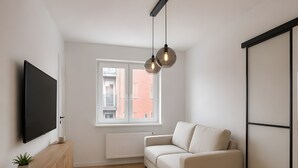 Un salon moderne doté d’un téléviseur à écran plat, d’un meuble en bois, d’un canapé beige et d’une grande fenêtre offrant une vue sur les immebles.