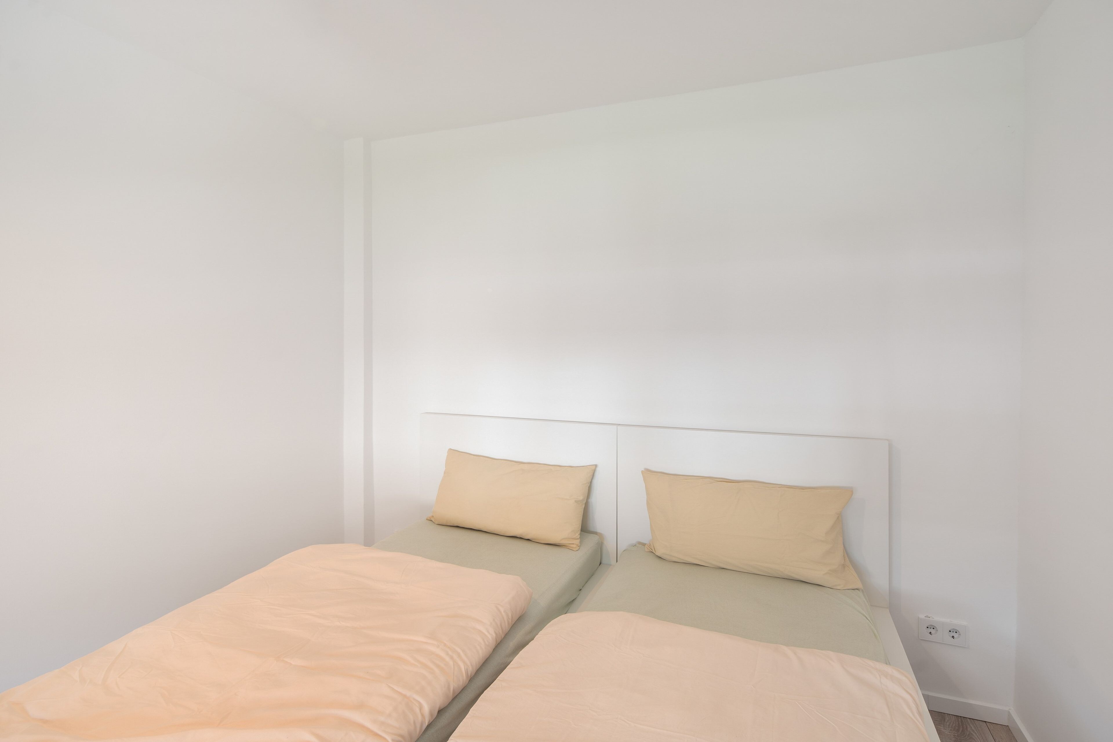 Une pièce simple et dépouillée, avec deux lits simples, chacun doté d’une tête de lit sobre et d’un seul oreiller.