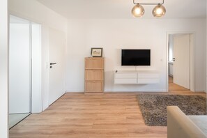 A modern living room with a flat-screen TV mounted on the wall, a wooden cabinet, and a fluffy rug. - Apartment 'Für 4 P. Küche & Wlan' with Wi-Fi (Dormagen)
