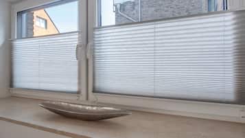 Una habitación con dos ventanas, cada una con una persiana blanca. Hay un objeto blanco en el alféizar.