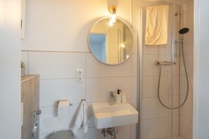 Un bany modern amb un mirall rodó, un lavabo, una barra de tovalloles i una dutxa.