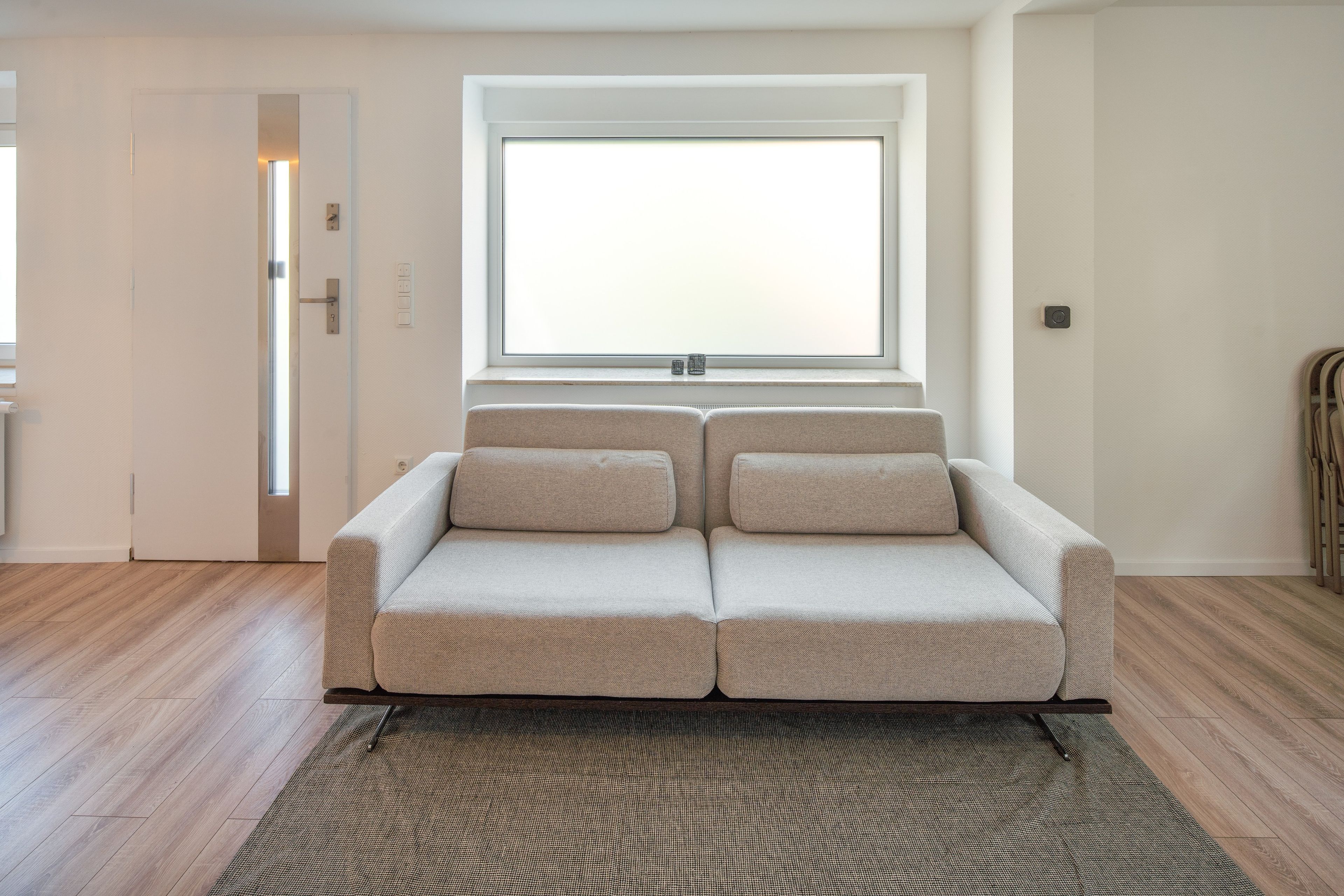 Ein modernes Wohnzimmer mit einer Couch, einem Fenster und einer Tür.