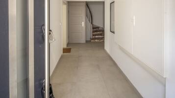 Un couloir avec une porte sur la gauche, un escalier au fond et un luminaire fixé au mur.