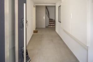 Passadís amb una porta a l'esquerra, una escala al fons i un llum penjant a la paret.