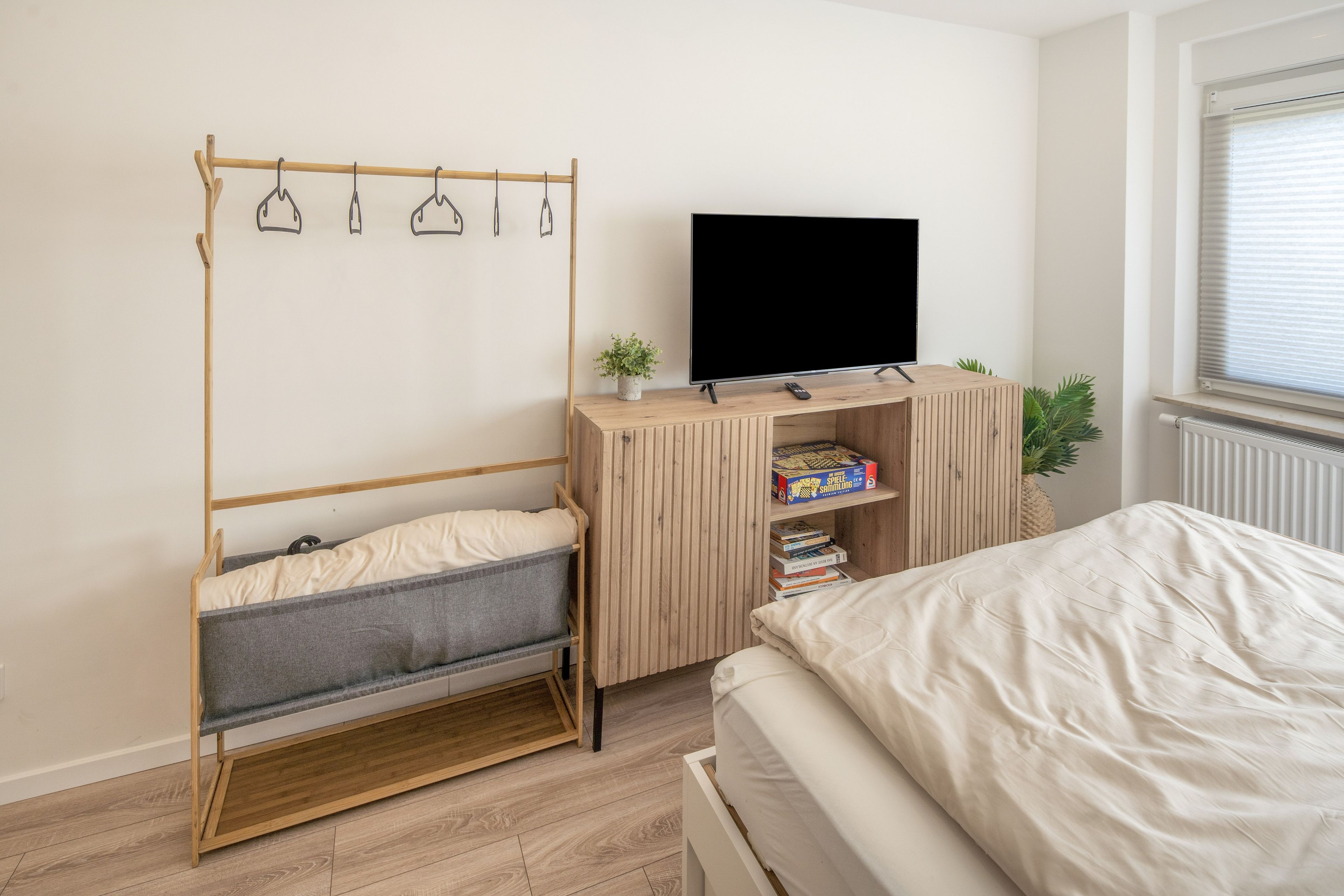 Ein Schlafzimmer mit einem Bett, einem Fernseher auf einem Holzboden, einem Bücherregal und einem Hängekorbstuhl.