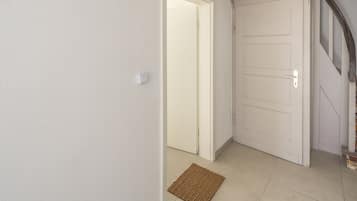 Un couloir avec un mur blanc à texture, une porte fermée et un paillasson marron sur le sol.