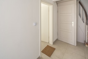 Un passadís amb una paret blanca amb relleu, una porta tancada i un felp de porta marró al terra.