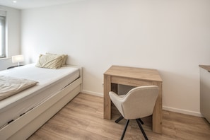 Une chambre à coucher minimaliste, avec un lit simple, une petite table en bois et une chaise.