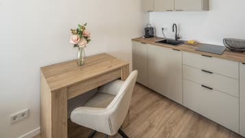 Une cuisine moderne avec un bureau en bois, une chaise, un vase avec des fleurs, une machine à café et un ordinateur portable.