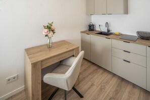 Una cuina moderna amb un escriptori de fusta, una cadira, un ram de flors, una cafetera i un ordinador portàtil.