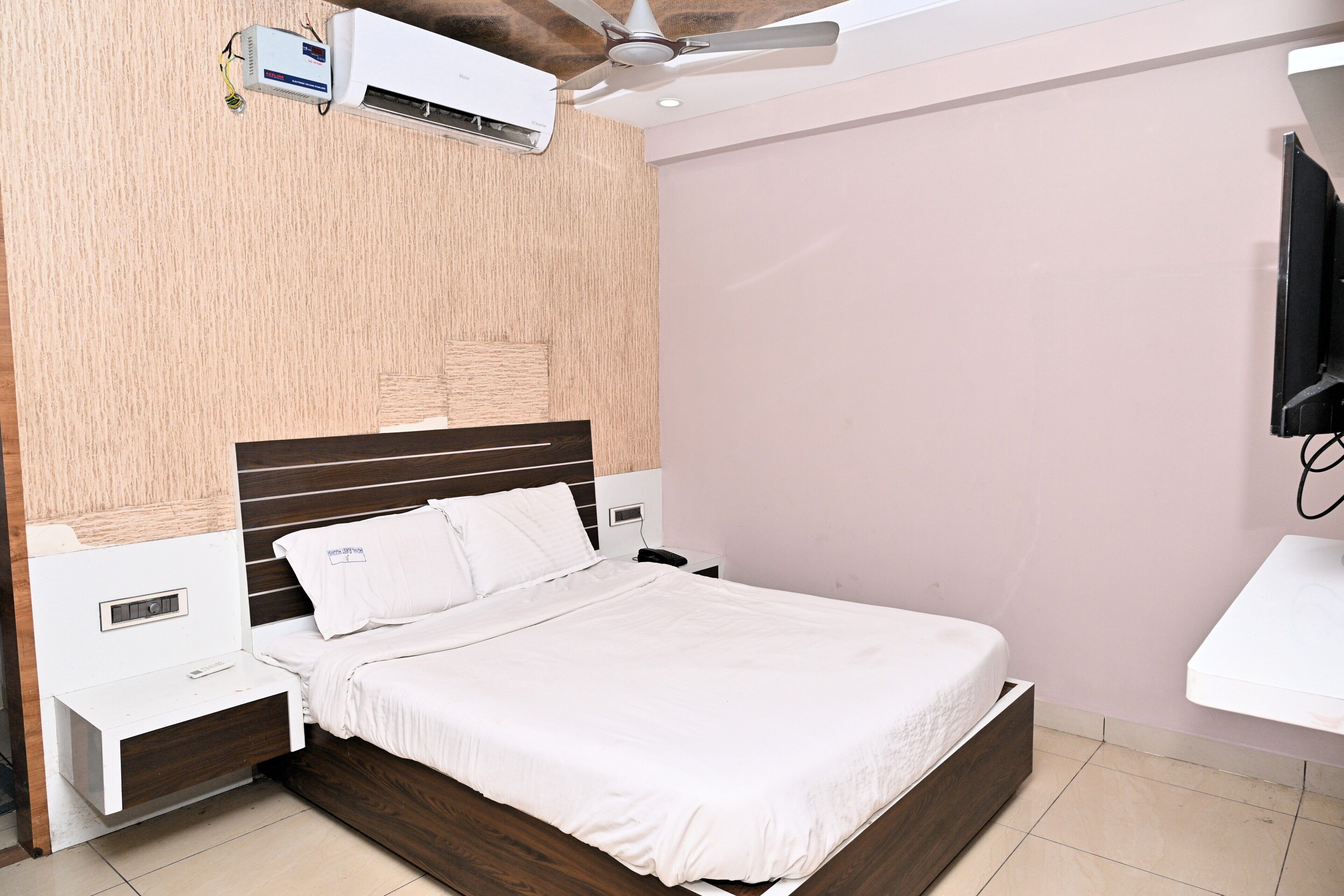 A hotel room with a bed, bedside tables, a wall-mounted air conditioner, and a ceiling fan.