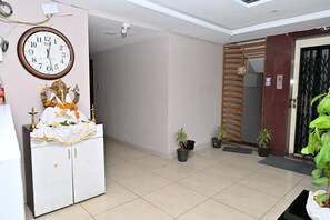 A room with a clock, a statue, a cabinet, and potted plants.