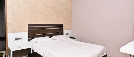 Una habitación de hotel con una cama individual, mesitas de noche, un escritorio y un equipo de aire acondicionado.