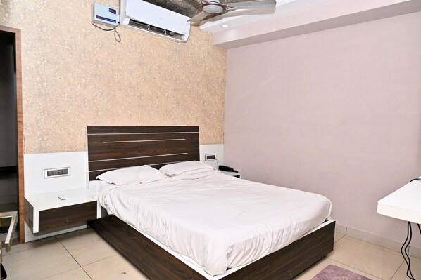 A hotel room with a single bed, bedside tables, a desk, and an air conditioning unit.