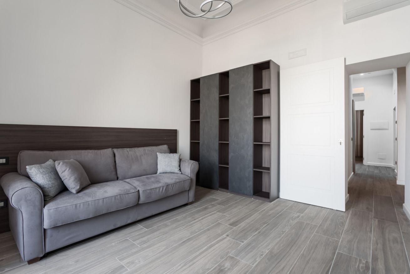 Un soggiorno moderno con un divano grigio, una parete attrezzata e una porta bianca che dà su un'altra stanza.