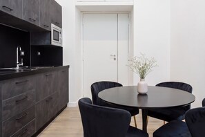 Eine moderne Küche mit dunklen Schränken, einer eingebauten Mikrowelle und einem Essbereich mit rundem Tisch und vier Stühlen.
