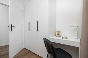 Una stanza minimalista con una scrivania bianca, una sedia, un quadro incorniciato e una lampada da scrivania.