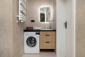 A compact bathroom with a washing machine, a sink, and a mirror. - Bright & Stylish Apartment with a Balcony | Parking | Workspace (Katowice)