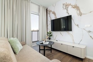 Un soggiorno moderno con un divano, un tavolino, una televisione fissata a una parete di marmo e un balcone visibile dalla finestra.