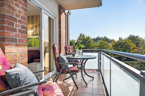 Un balcon avec une table et des chaises, un canapé et une vue sur les arbres et les bâtiments.