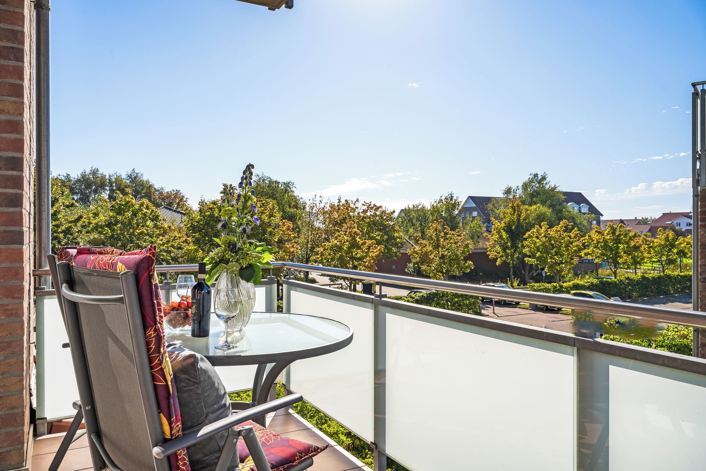 A balcony with a chair, a table, and a vase with flowers.