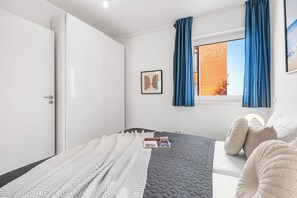 Ein Schlafzimmer mit einem Bett, einem Fenster mit Vorhängen, einer Tür und einem an der Wand hängenden Bild.