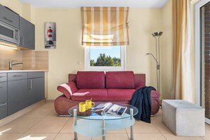 Ein gemütlicher Wohnbereich mit Küchenzeile, einer Couch, einem Glastisch und einem Fenster mit Blick.