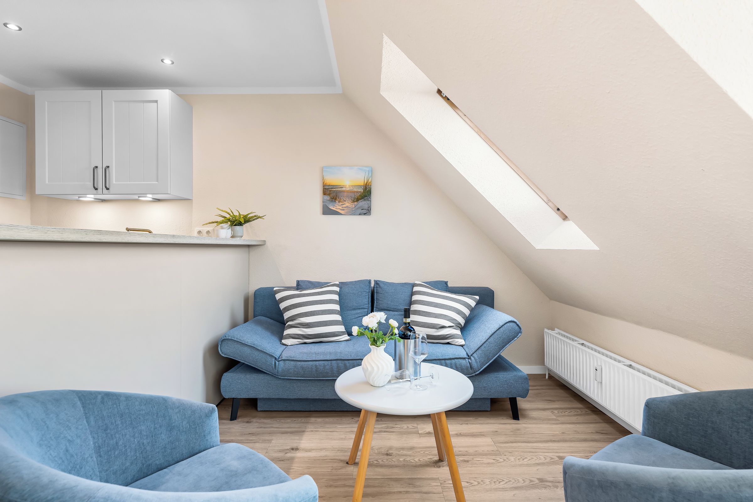 A modern living space with a blue sofa, two armchairs, a small white table, and a painting of a sunset.