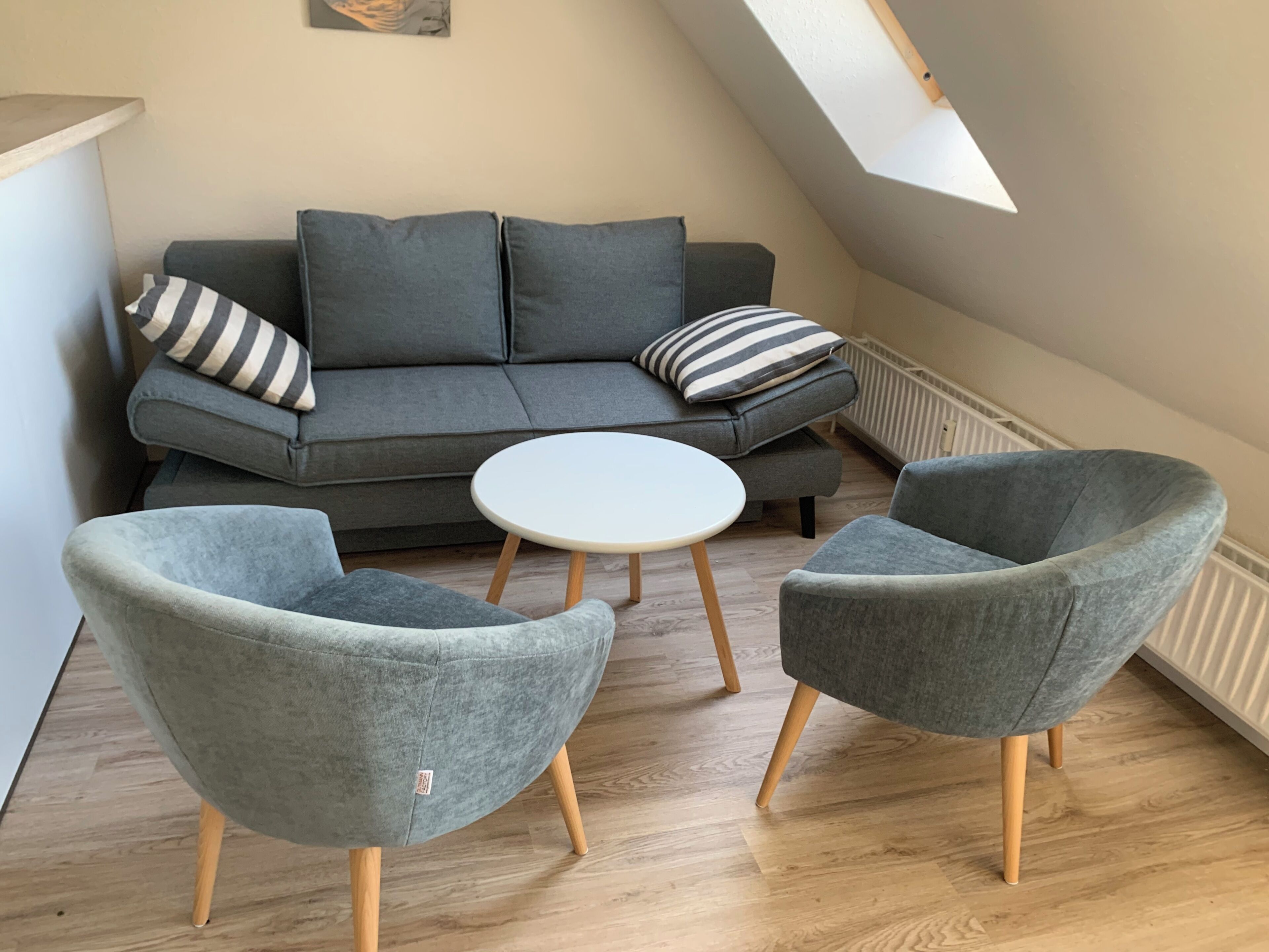 Una sala moderna con un sofá gris, dos sillones, una mesita blanca y un tragaluz.