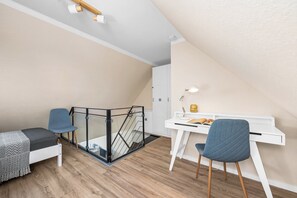 A modern loft bedroom with a sloped ceiling, a glass balcony, a desk with a chair, and a bed with a blanket. - Holiday Apartment Strandblick – Sea Views, Relaxation & Holiday Bliss (Schönberg (Holstein))