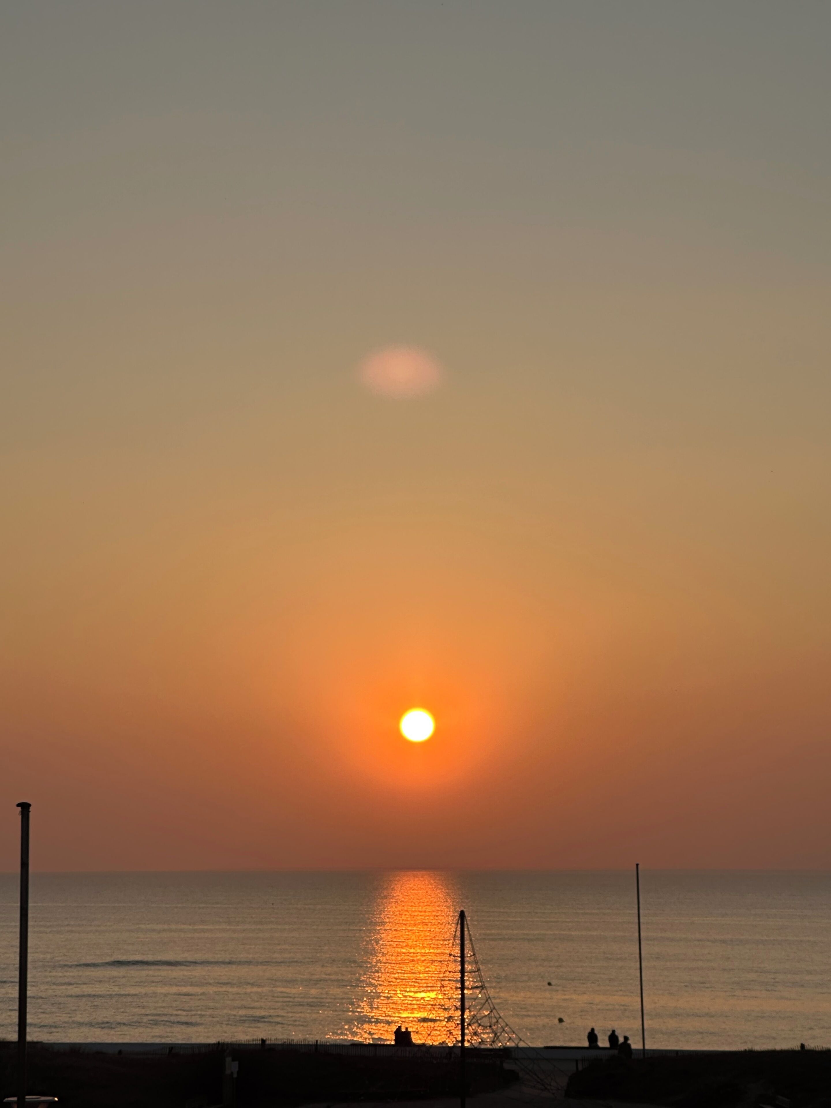 Een zonsondergang boven een rustige zee, met een pier die het water in reikt.