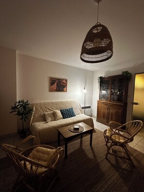 A living room with a sofa, two chairs, a coffee table, a hanging light fixture, a cabinet, and a plant. - T1 Bis-style studio with a large terrace overlooking the ocean (saint hilaire de riez)