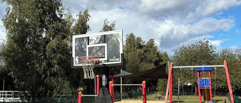 A basketball court with a Spalding hoop, a swing set, and a fenced playground area.