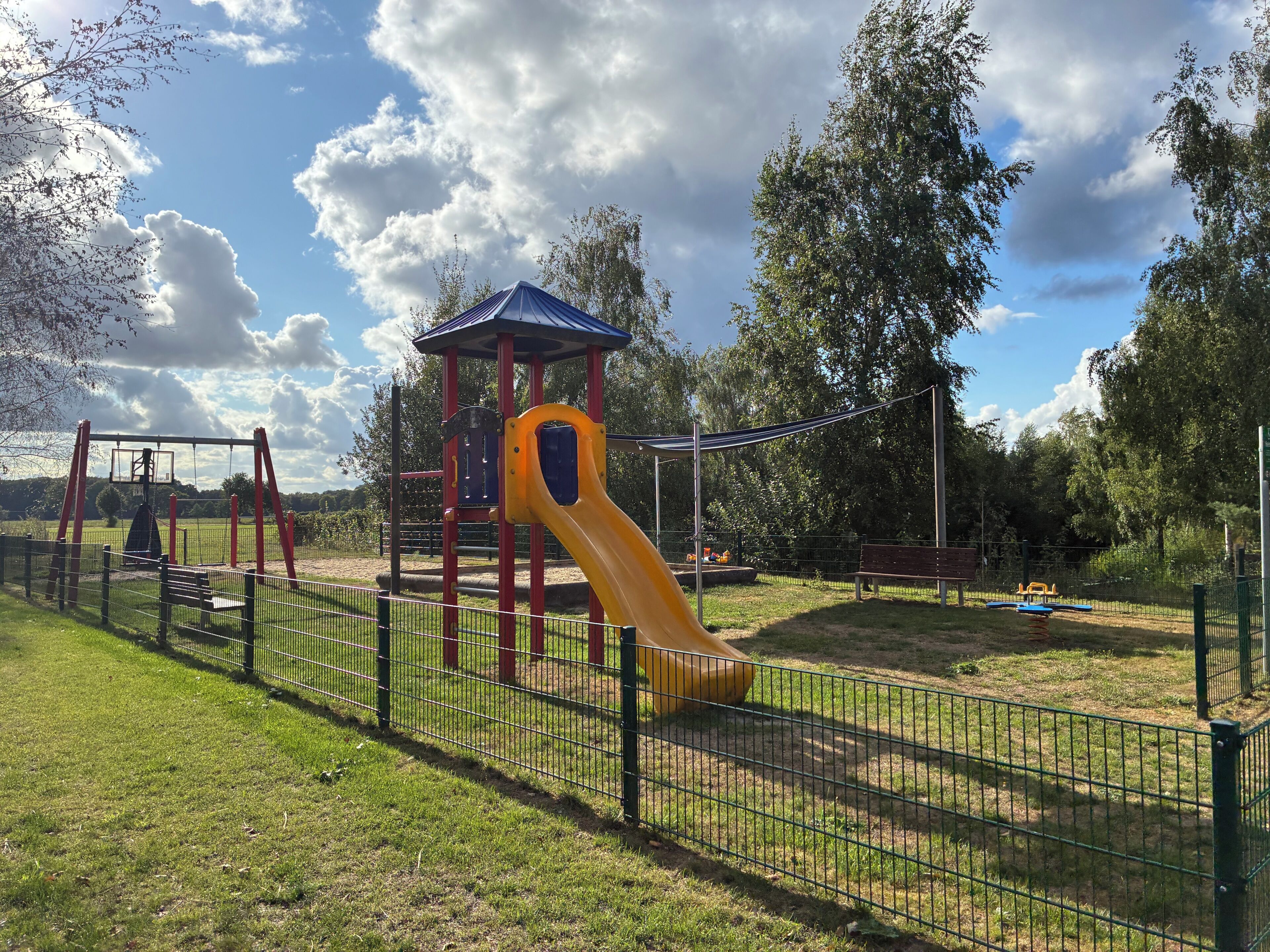 Ein Spielplatz mit einer gelben Rutsche und einer Kletterkonstruktion, umzäunt.