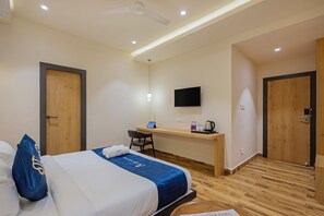 Ein Hotelzimmer mit Bett, Schreibtisch, Stuhl, Fernseher und Deckenventilator.