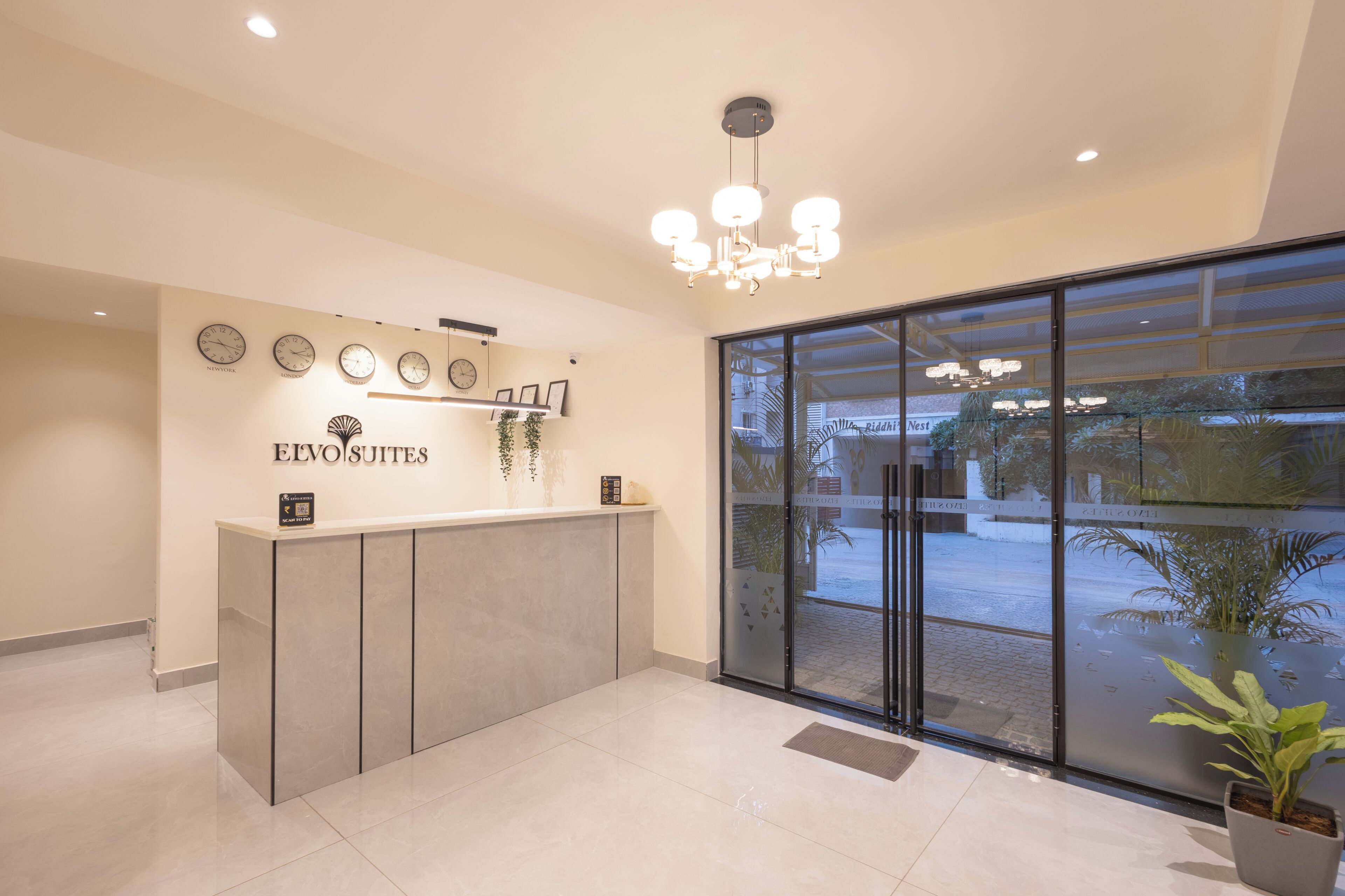 A reception desk with clocks, a chandelier, and a view of the outside.