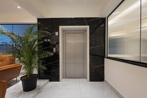 Un ascenseur moderne avec un mur en marbre noir, une plante en pot et un fauteuil en cuir.