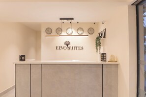 Un comptoir d’accueil avec des horloges indiquant différents fuseaux horaires, un logo pour «EVOJITES», et un code QR à scanner.